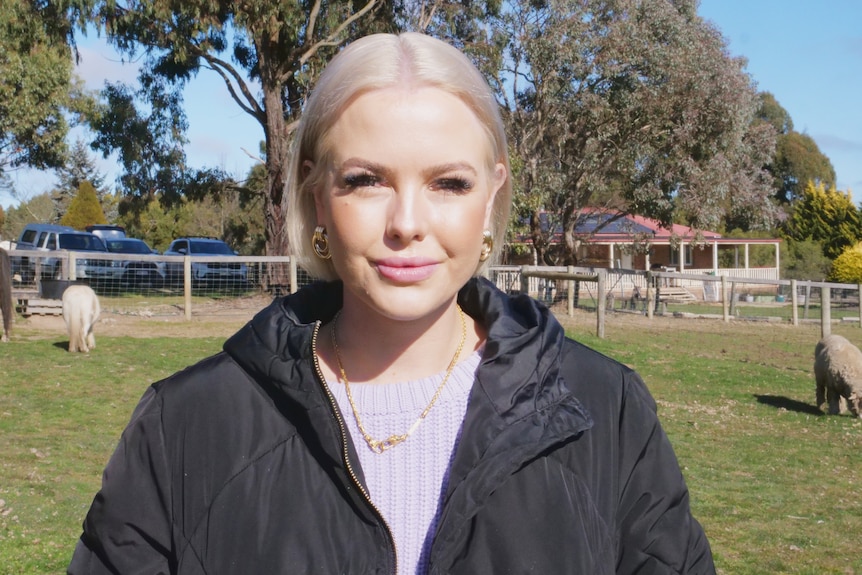 A lady with white blonde hair stands in a paddock