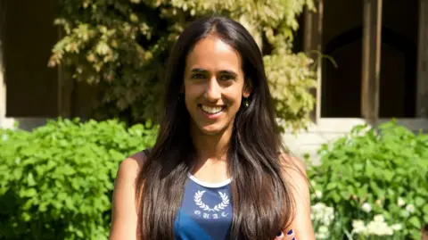 Steward Humble Smiling Anika Schwarze-Chintapatla, wearing athletics gear outside her Oxford University college