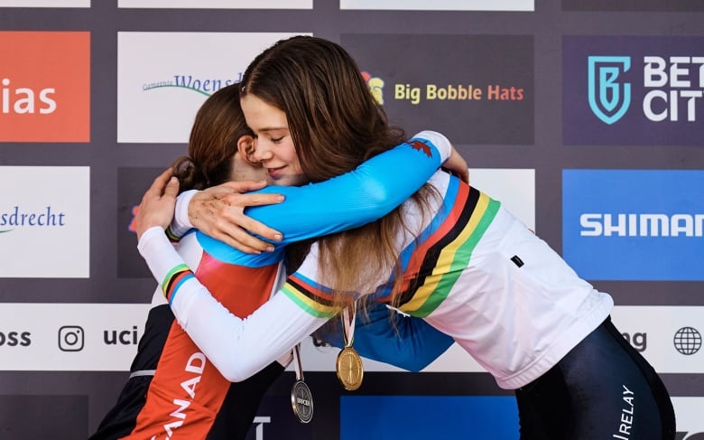 Isabella Holmgren, in champion's rainbow jersey, hugs silver-winning sister Ava Holmgren on the Cyclo-Cross podium at Hoogerheide, the Netherlands. Feb 2023