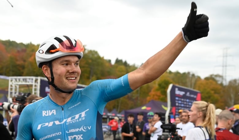 A man in a bicycle helmet and racing uniform offers a thumbs up to the crowd.