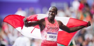 Marco Arop smiles with the Canadian flag flowing behind him