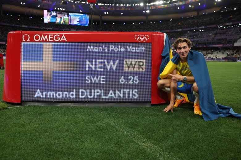 A male athlete poses beside a digital screen showing the world record he had just set.