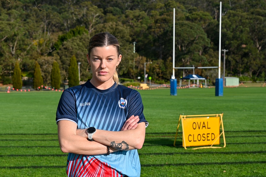 A woman stands in front of an oval with her arms crossed. There is a sign that reads ‘oval closed’. 