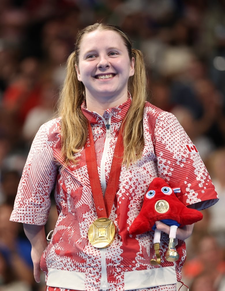 A female Paralympic swimmer smiles while posing with a gold medal around her neck.