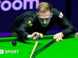 Judd Trump plays a shot, using the rest