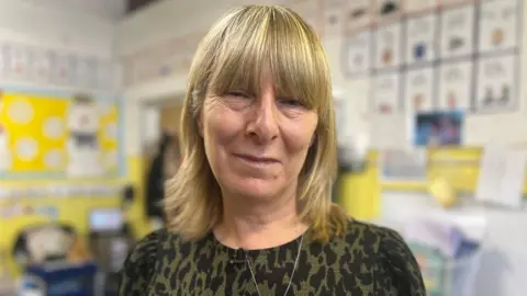 Sue Lewis smiling into the camera. She is wearing a black and green animal print top. She has blonde mid-length hair with a fringe.