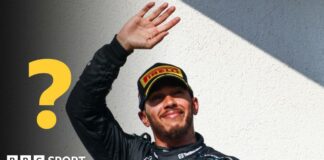 Lewis Hamilton waves while wearing a Mercedes race uniform. A question mark graphic is to the left of the image