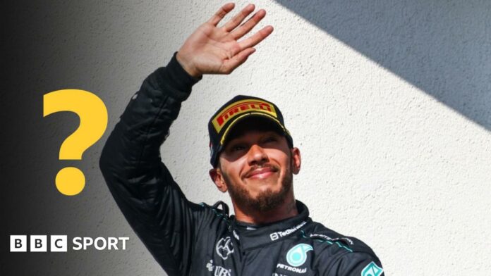 Lewis Hamilton waves while wearing a Mercedes race uniform. A question mark graphic is to the left of the image