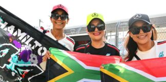 Three Formula 1 fans wear Mercedes branded caps and hold up South African flags and a banner reading 'Hamilton 44'