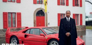 Lewis Hamilton stood alongside a Ferrari sports car while wearing a black suit and black overcoat