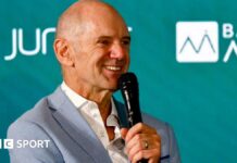 Adrian Newey speaking into a microphone at an Aston Martin news conference