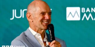 Adrian Newey speaking into a microphone at an Aston Martin news conference