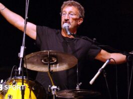 Eddie Jordan with his arms outstretched while playing the drums