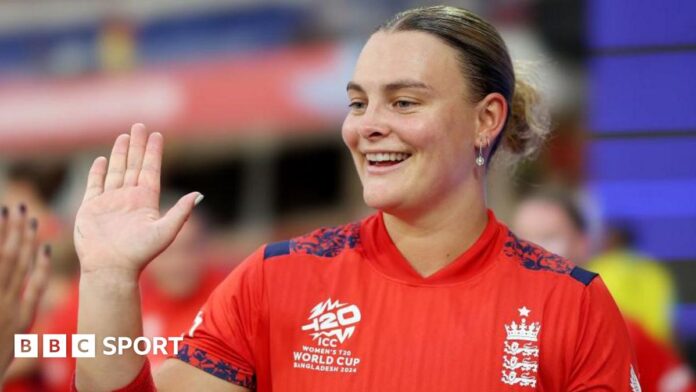 Danielle Gibson holds up her palm and is wearing a red England cricket shirt