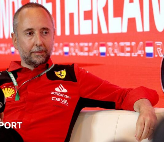Enrico Cardile wearing a Ferrari top and holding an FIA-branded microphone